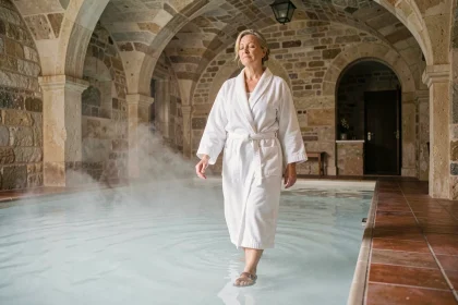 Senior active en robe de bain blanche entrant dans une piscine thermale minérale dans un établissement thermal traditionnel français